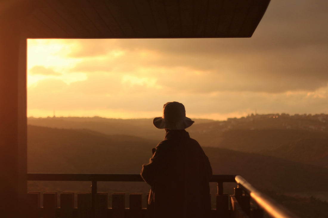 Woman silhouetted against a golden sunset on a mountain balcony, representing the well-traveled mom who moves through the world with intention.